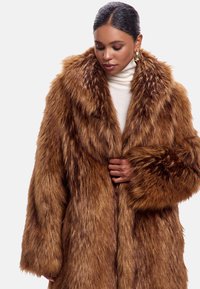 Brun faux fur frakke med en tykk, shaggy tekstur, bred krave og oversized ærmer. Designet har en frontlukning med en blød foring.