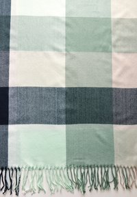 Couverture à carreaux dans des nuances de vert et de bleu marine. Texture douce avec des bords frangés. Présente de grands carrés de différentes teintes.