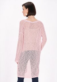 Rosa gestrickter Pullover mit lockerer, offener Maschenstruktur, langen Ärmeln und rundem Ausschnitt. Der Rücken ist länger als die Vorderseite und hat seitliche Schlitze.