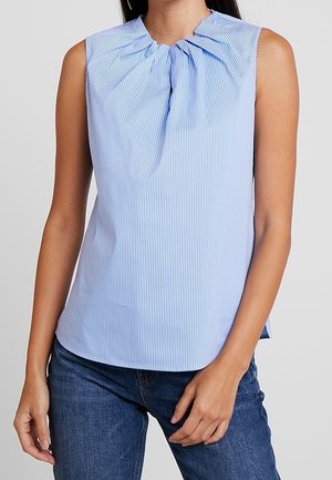 Sleeveless light blue and white striped blouse with gathered neckline, worn with blue denim jeans on a standing person.