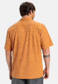 Short-sleeve shirt in textured orange fabric featuring a pattern of raised squares with circular motifs. Classic collar and straight cut.