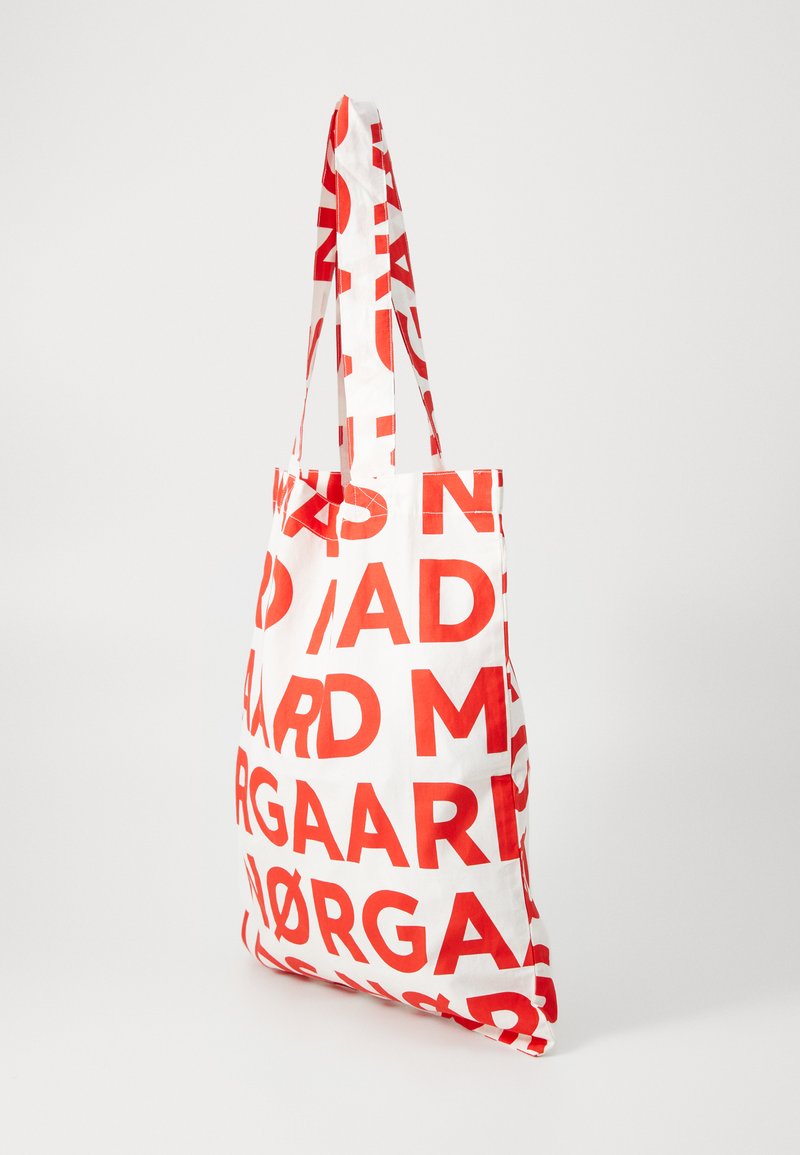 Bolsa de lona con fondo blanco y gran texto rojo. Cuenta con dos correas de hombro a juego y una forma estructurada.