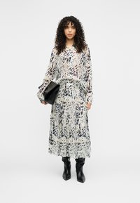 Σετ με μπλούζα μακρυμάνικη και φούστα maxi, με τύπωμα σε λευκό και μαύρο που θυμίζει πιτσιλιές. Το ύφασμα είναι ελαφρύ και αέρινο. Συνδυάζεται με μαύρα μπότες με τακούνι.