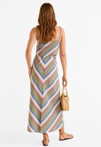 Robe maxi avec un motif en chevrons dans des couleurs pastel, fabriquée en tissu léger. Dotée de fines bretelles et d'une taille ceinturée. Portée avec un sac en osier.