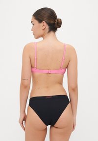 Rózsaszín csíkos bikini felsőrész állítható pántokkal, fekete, magas derekú alsósrész, amelyen piros "ROXY" felirat található a derékrészen.