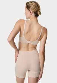 Beige beha met verstelbare banden en haaksluiting, gecombineerd met gladde, hoge shorts in dezelfde kleur, beide gemaakt van rekbaar materiaal.