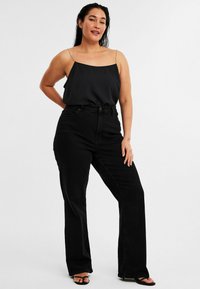 Svart satin cami-top med guldkedjor, bärs med högmidjade svarta jeans. Outfiten har en avslappnad passform och en smidig textur.