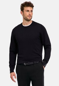 Maglione nero a collo rotondo con maniche lunghe, realizzato in tessuto morbido. Presenta un colletto interno bianco e un piccolo dettaglio con logo sulla manica.
