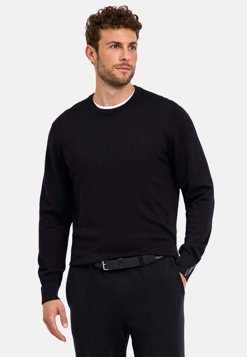 Maglione nero a collo rotondo con maniche lunghe, realizzato in tessuto morbido. Presenta un colletto interno bianco e un piccolo dettaglio con logo sulla manica.
