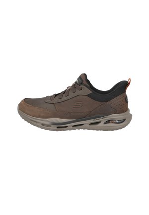Zapatilla marrón y negra con cierre de cordones, suela acolchada gruesa y marca "Arch Fit" en el lateral para mayor soporte del arco y confort.