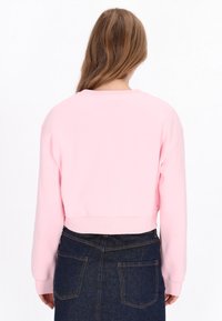 Rózsaszín, rövidített hosszú ujjú pulóver bordázott mandzsettával, magas derekú farmer szoknyával párosítva, egyszerű és letisztult dizájnt mutatva.