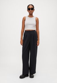 Gray cropped tank top, high-waisted black pleated wide-leg trousers, black chunky platform shoes with silver studs, and dark sunglasses.