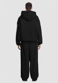 Czarna, oversize bluza z dużym kapturem, prążkowanymi mankietami i luźnym krojem, zestawiona z luźnymi czarnymi spodniami. Prosty design, bez wzorów.