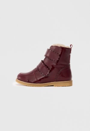 Bottes bordeaux mi-mollet avec finition brillante, dotées de deux sangles ajustables et d'une doublure en fourrure douce de couleur crème. Détails texturés sur les côtés.