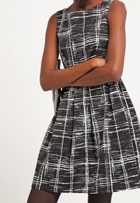 Sorte og hvide ærmeløse kjole med rutenet mønster, plisseret skørt og rund halsudskæring. Glat stof med en struktureret pasform.