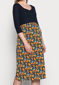 Šaty s námořnickým žebrovaným vrškem a květinovou sukní s oranžovými a modrými květy na tmavém pozadí. Úzký střih, délka k kolenům.