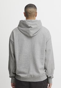 Hoodie in Hellgrau mit weichem Stoff, lockerer Passform und gerippten Bündchen und Saum. Von hinten gesehen, mit einem schlichten Design.