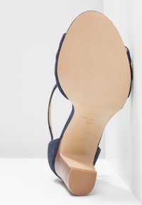 Chaussure à talons hauts en daim bleu marine avec une semelle en cuir lisse, ouverte à l'arrière, et un design de bracelet délicat autour de la cheville. Taille 37 marquée sur la semelle intérieure.