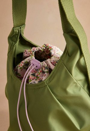 Grüne Stofftasche mit Kordelzugverschluss und floralem Innenfutter. Verfügt über breite Träger und eine glatte Textur.