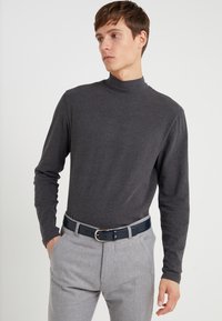 Camisa de cuello alto gris de manga larga hecha de tela suave, combinada con pantalones claros grises y un cinturón de cuero azul oscuro con una hebilla plateada.