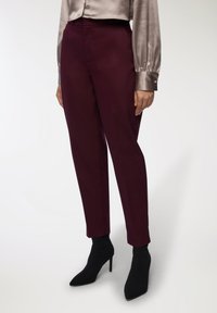 Burgundowe spodnie dopasowane z gładkiego materiału, wysoki stan i zwężona nogawka. Noszone z jedwabną szaro-bluzą i czarnymi szpilkami za kostkę.