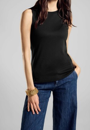 Zwarte mouwloze top gemaakt van gladde stof, gecombineerd met losse blauwe denim jeans. Een transparante beige armband siert de pols.