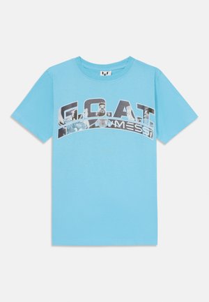 Camiseta de algodón azul claro con un estampado gráfico de la palabra "G.O.A.T." y imágenes, con cuello redondo y mangas cortas.