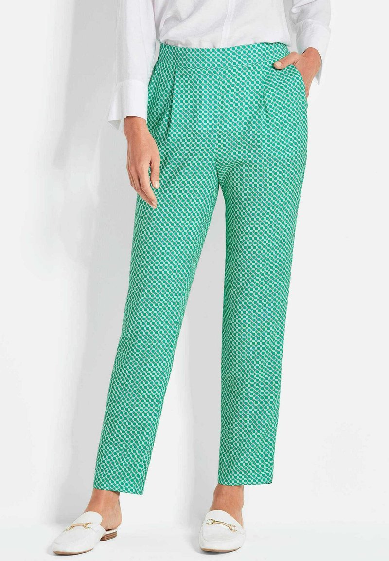 Grüne gemusterte Hose mit geometrischem Design, ausgestattet mit Falten, seitlichen Taschen und einer taillierten Passform, kombiniert mit weißen Slippern.