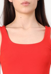 Red ribbed tank top with a square neckline, wide straps, and smooth texture, showcasing a fitted design for a streamlined silhouette.