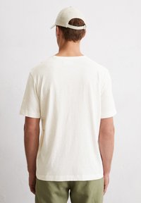 Kurzärmliges, cremefarbenes T-Shirt aus weichem Material, mit Rundhalsausschnitt und lässiger Passform, getragen mit grüßen Hosen.
