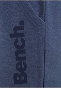 Dunkelblaue Kapuzenjacke mit einem auffälligen schwarzen "Bench."-Logo an der Seite, aus einem weichen, strukturierten Stoff mit einer Fronttasche.