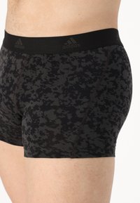 Fekete és szürke mintás boxer alsónadrág, elasztikus derékpánttal, amelyen az Adidas logó található, sima anyaggal és testhezálló kialakítással.
