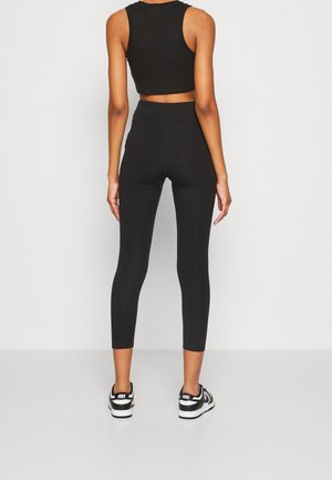 Persoon die met de rug naar voren staat, draagt een zwart cropped tanktop, hoge taille zwarte legging en zwart-witte Nike sneakers.