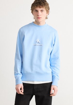Lichtblauwe sweatshirt met geribbelde manchetten en zoom, voorzien van een witte geborduurde "CK"-logo en de tekst "Calvin Klein Jeans" op de borst.