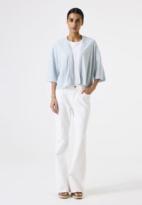 Lichtblauwe cropped jas met een open voorkant, brede mouwen en een zachte textuur, gecombineerd met witte flared broek en bruine plateausandalen.