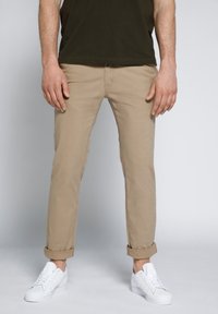 Chino beige con orli arrotolati, realizzati in un morbido misto cotone, abbinati a sneakers bianche. Il design presenta tasche standard e passanti per la cintura.