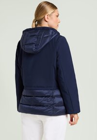 Marineblauw jack met een capuchon, voorzien van een doorgestikte onderkant en een gladde bovenstof. Zachte textuur, getailleerde pasvorm en geen zichtbare sluitingen.