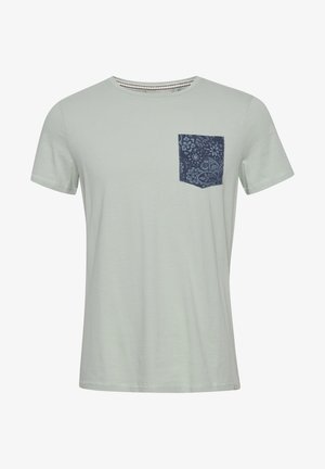 T-shirt vert clair avec un col rond, des manches courtes et une poche à motif bleu marine sur le côté gauche. Texture douce et lisse.