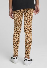 Leggingi z vzorcem leoparda v rjavo in bež barvni shemi, izdelani iz elastičnega blaga, z oprijetim krojem in gladko teksturo.
