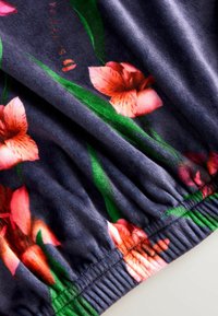 Lillemustriga kangas, millel on roosad ja oranžid lilled tumesinisel taustal, koos voltide ja kummikujulise äärega.