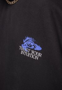 Black cotton t-shirt featuring a blue graphic of an eye above the text "TRUST YOUR INTUITION" in white. Smooth texture, casual design.
