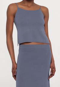 Gray ribbed knit crop top with thin straps. Tailored fit, slightly cropped design, paired with a matching skirt. Smooth texture.