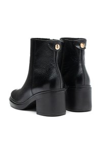 Par svarta läderankelboots med klossklackar, strukturerad yta, sidodragkedjor och små guldknappar som detalj vid toppkanterna.