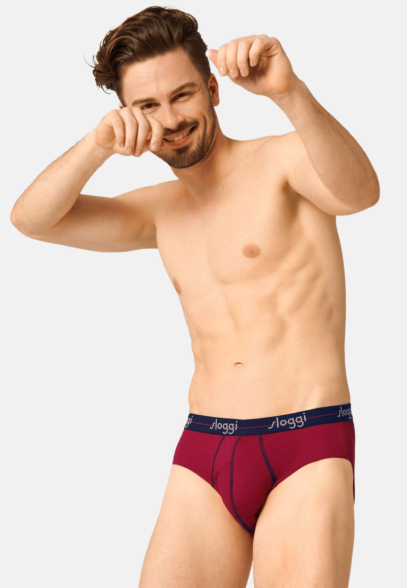 Bordeauxrote Unterwäsche in Form eines Slips mit einem marineblauen Gummibund, der das "sloggi"-Logo trägt, flachen Nähten und einem konturierten Vordesign.