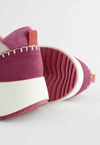 Violet nubuk sneaker dengan sol tengah putih, outsole karet bertekstur, dan tab tumit oranye. Desain dua warna menampilkan jahitan kontras.