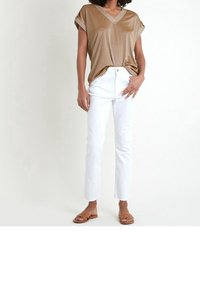 Person wearing metallic gold short-sleeve V-neck top, white high-waist straight-leg jeans, and brown flat sandals on a white background.