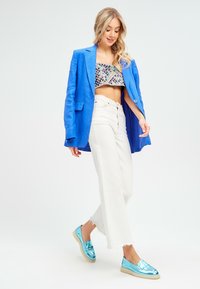 Blazer aus blauer Leinen, gekürztes Paillettenoberteil, weiße weit geschnittene Hose und glänzende türkisfarbene Slipper. Lässiges Outfit mit unterschiedlichen Texturen und Farben.