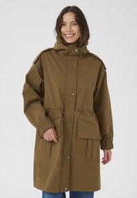 Bruine, lichte parka met een capuchon, trekkoord in de taille, drukknoopjes en twee voorzakken; heeft elastische manchetten en schouderepauletten.