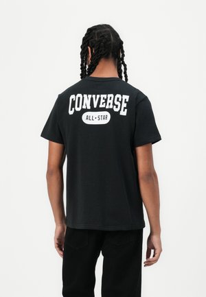 Must must kampsärk, millel on seljal suur valge "CONVERSE" ja "ALL★STAR" tekst; lühikesed varrukad, lõdva lõikega, lihtne seljaosa disain.