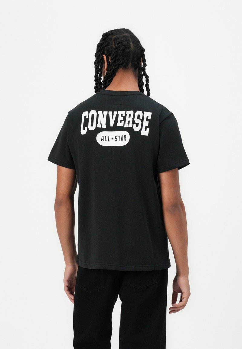 Juodas medvilninis marškinėliai su dideliu baltu užrašu "CONVERSE" ir "ALL★STAR" ant nugaros; trumpomis rankovėmis, laisvas kirpimas, paprastas nugaros dizainas.